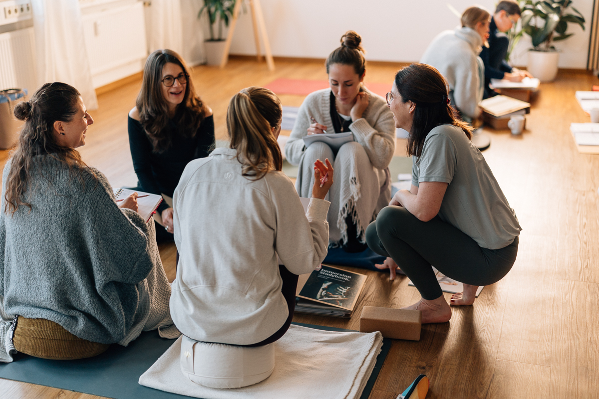 Eine Gruppe Yogalehrenden arbeitet gemeinsam in der Gruppe und wird von Ausbilderin Sabine Willmann unterstützt.